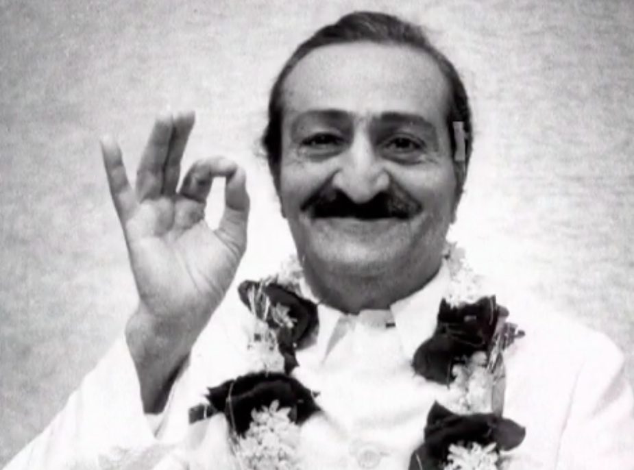 A man with mustache and lei giving the peace sign.